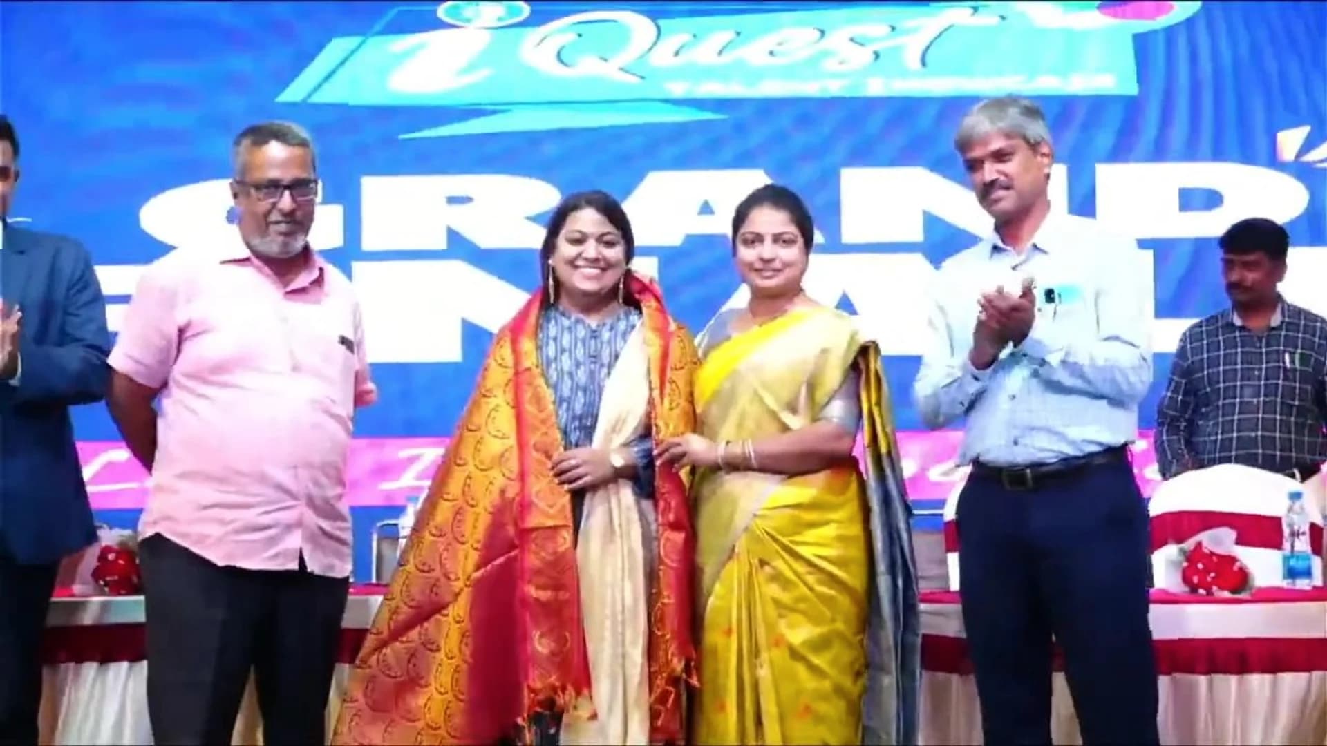 Pushpavalli being honoured with a ceremonial shawl on stage at an iQuest event.