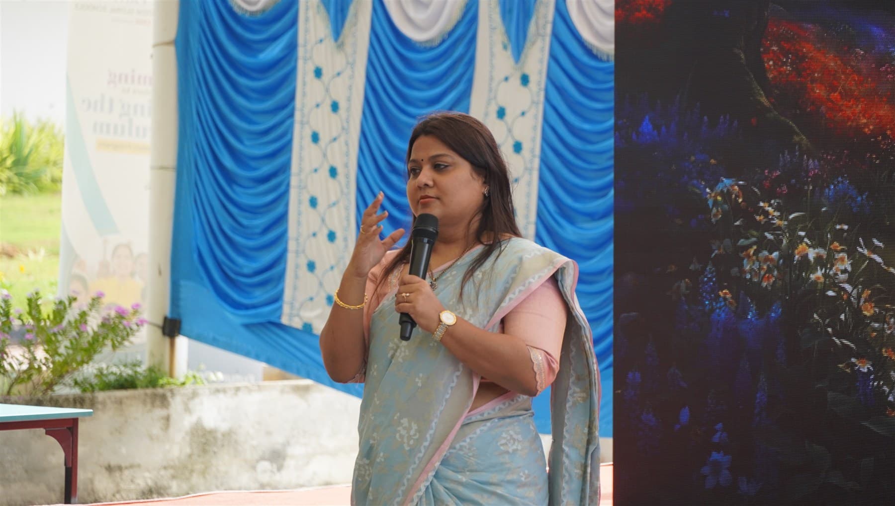 Pushpavalli speaking into a microphone at an education programme.